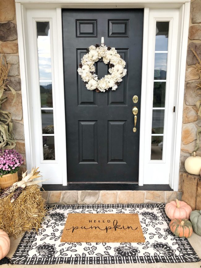 Black door with a white fall wreath and a doormat that says "hello, pumpkin"