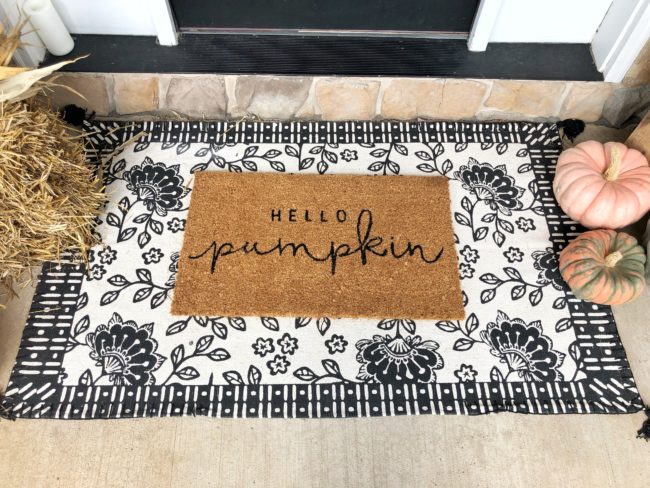 A doormat that says "hello, pumpkin" layered on a black and white floral area rug