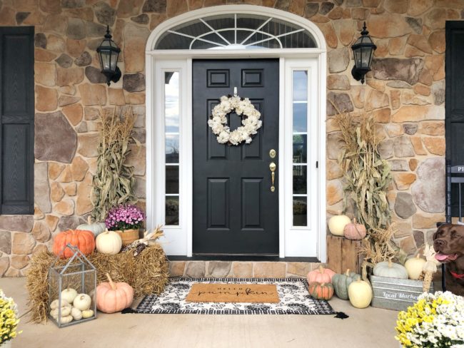 A front porch decorated for fall, with hay bales, cornstalks and pumpkins